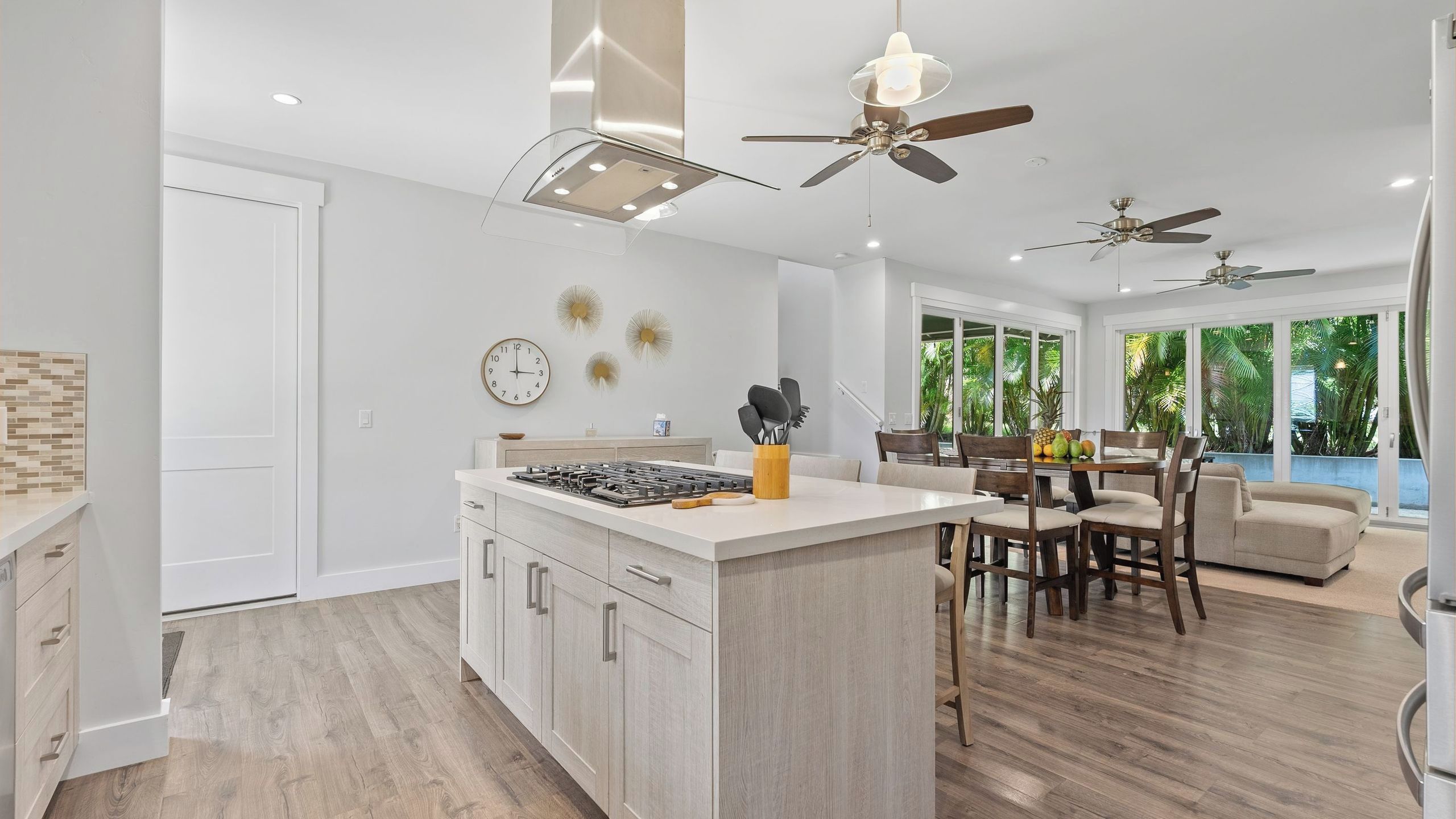 A modern kitchen with a central island, dining area with chairs, and ceiling fans.