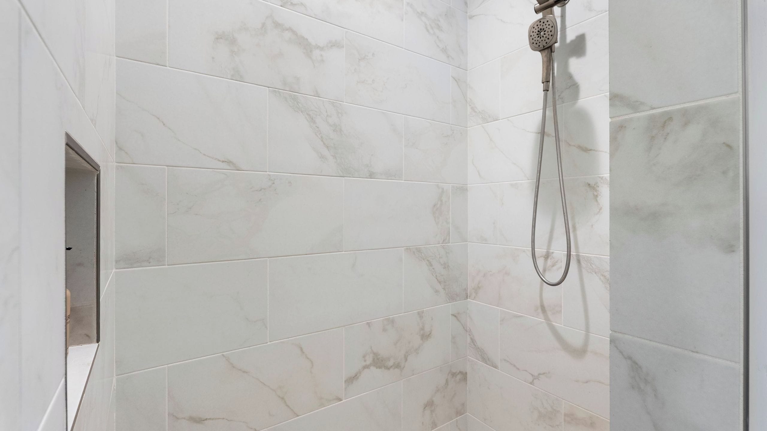 A bathroom with white marble tiles and a shower head.