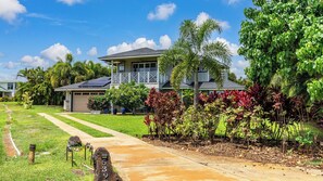 A two-story house with a covered porch, surrounded by lush greenery and a well-maintained lawn. - Hale Pōmaikai by Avantstay Ocean View Lanai + Covered Dining Minutes to Poipu Beach & Koloa (Koloa)