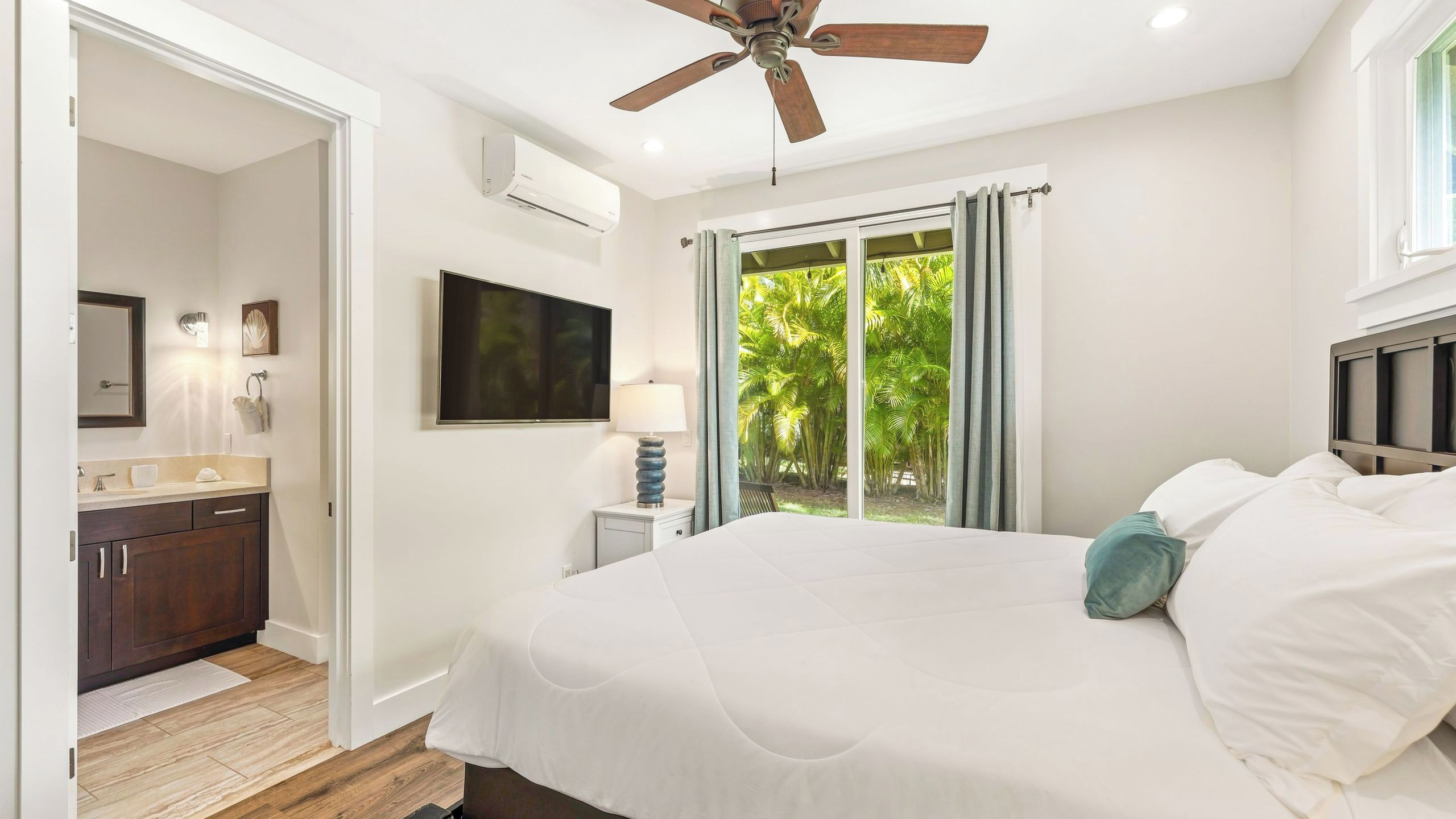 A bedroom with a bed, a ceiling fan, a TV, and a window with curtains.