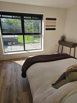 Une chambre avec une grande fenêtre, un lit, une petite table et une étagère fixée au mur.