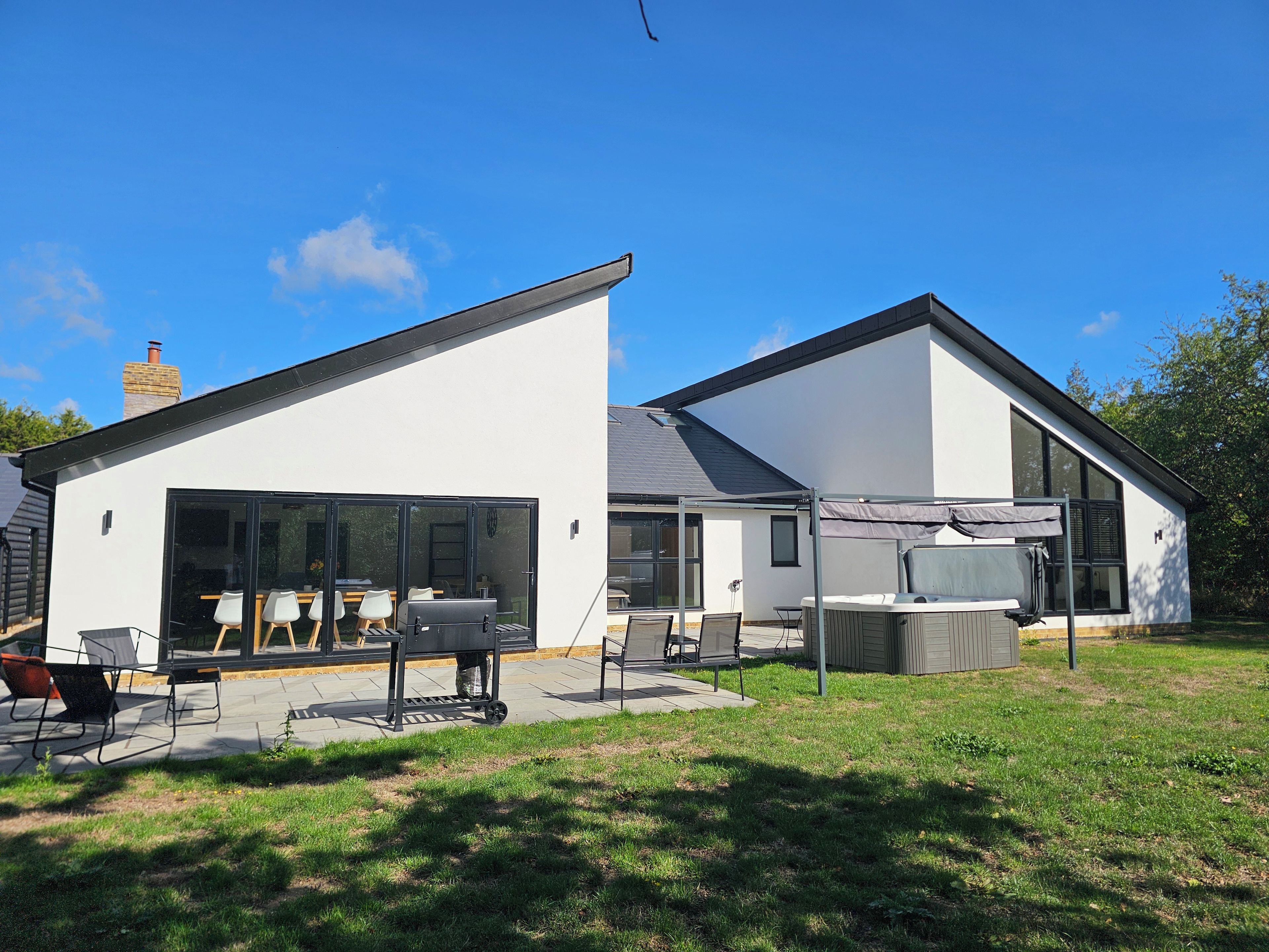 Een modern huis met twee verdiepingen, een patio, grote ramen en een zichtbare schoorsteen.