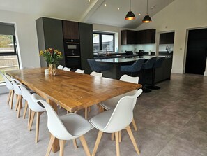 A modern kitchen with dark cabinetry, a wooden dining table, and white chairs.