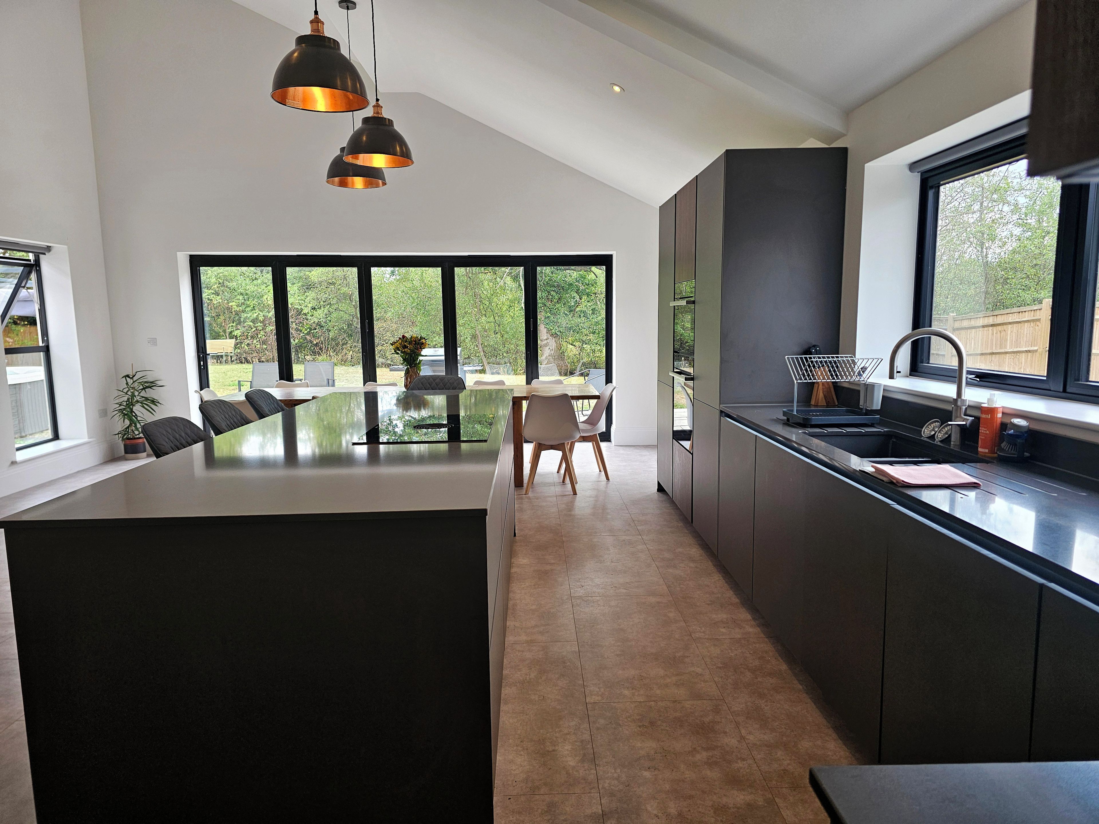 A modern kitchen with a large island, dark cabinetry, and pendant lighting.