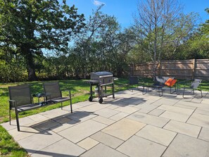 Un patio exterior con una parrilla, dos sillas y una mesa.