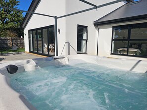 A hot tub with a clear view of the surrounding patio area, including a seating arrangement and a building with large windows.