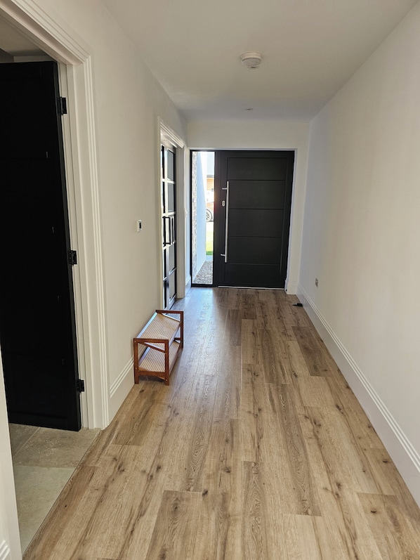 Un couloir doté d’un plancher en bois, d’un banc et d’une porte donnant sur un espace extérieur.