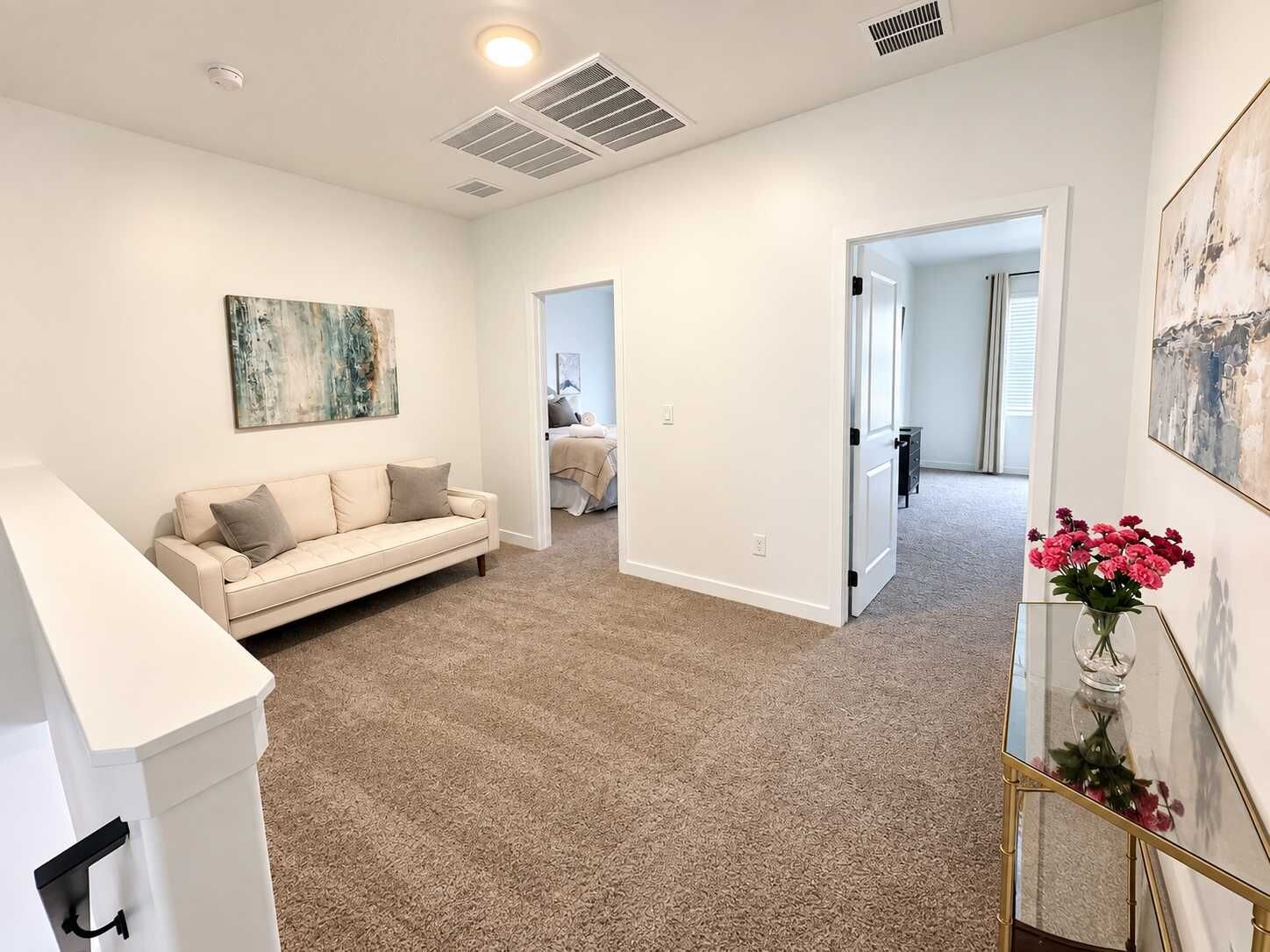 A spacious living room with a beige carpet, a white sofa, and a painting on the wall.