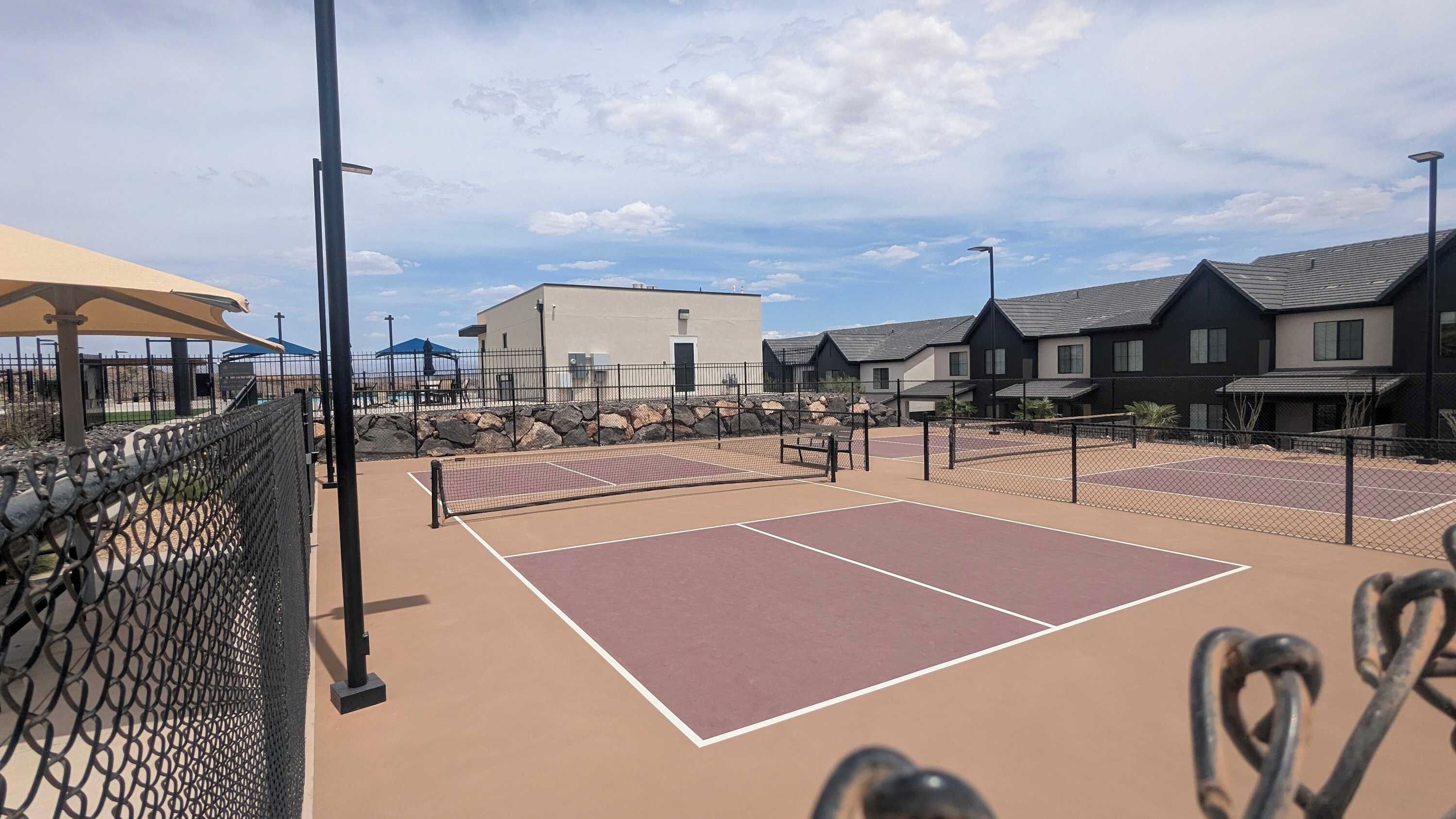 A tennis court with a net, surrounded by a fence, and adjacent buildings.