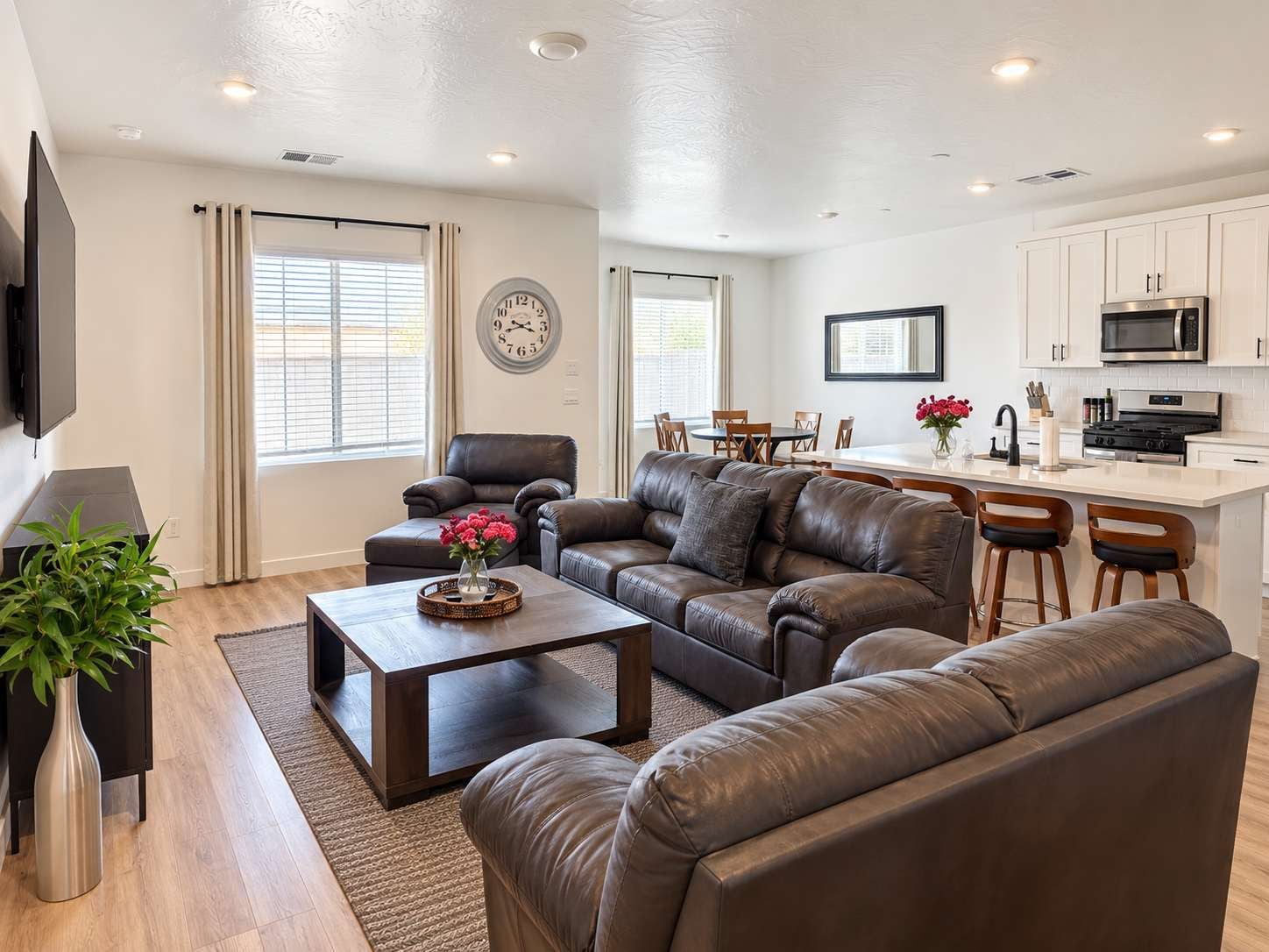 A modern living room with leather sofas, a coffee table, and a TV. There is a kitchen area with white cabinets and a microwave.