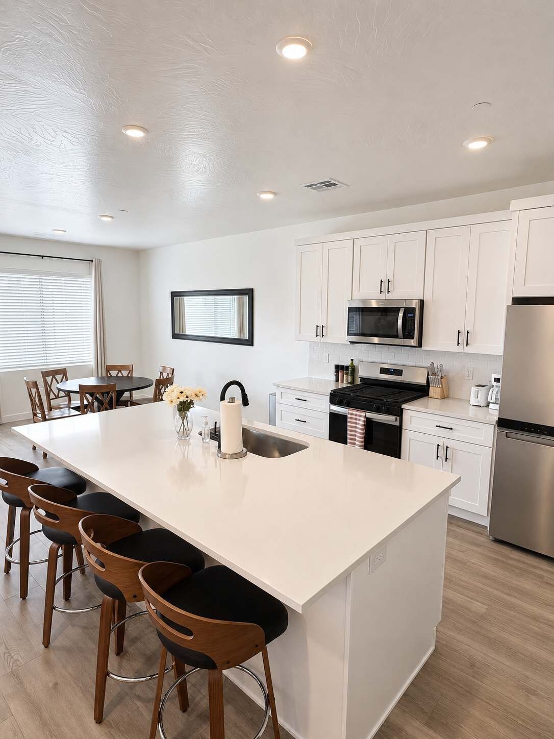 A modern kitchen with white cabinetry, a central island with bar stools, a stainless steel refrigerator, and a microwave.