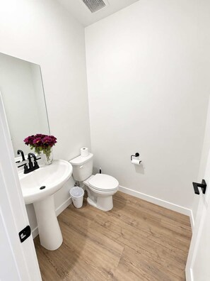 Une salle de bain avec un lavabo, des toilettes et un miroir, le tout de couleur blanche.