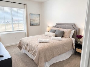 Une chambre à coucher avec un lit, une table de chevet, une lampe, un tableau au mur et une fenêtre avec des stores.
