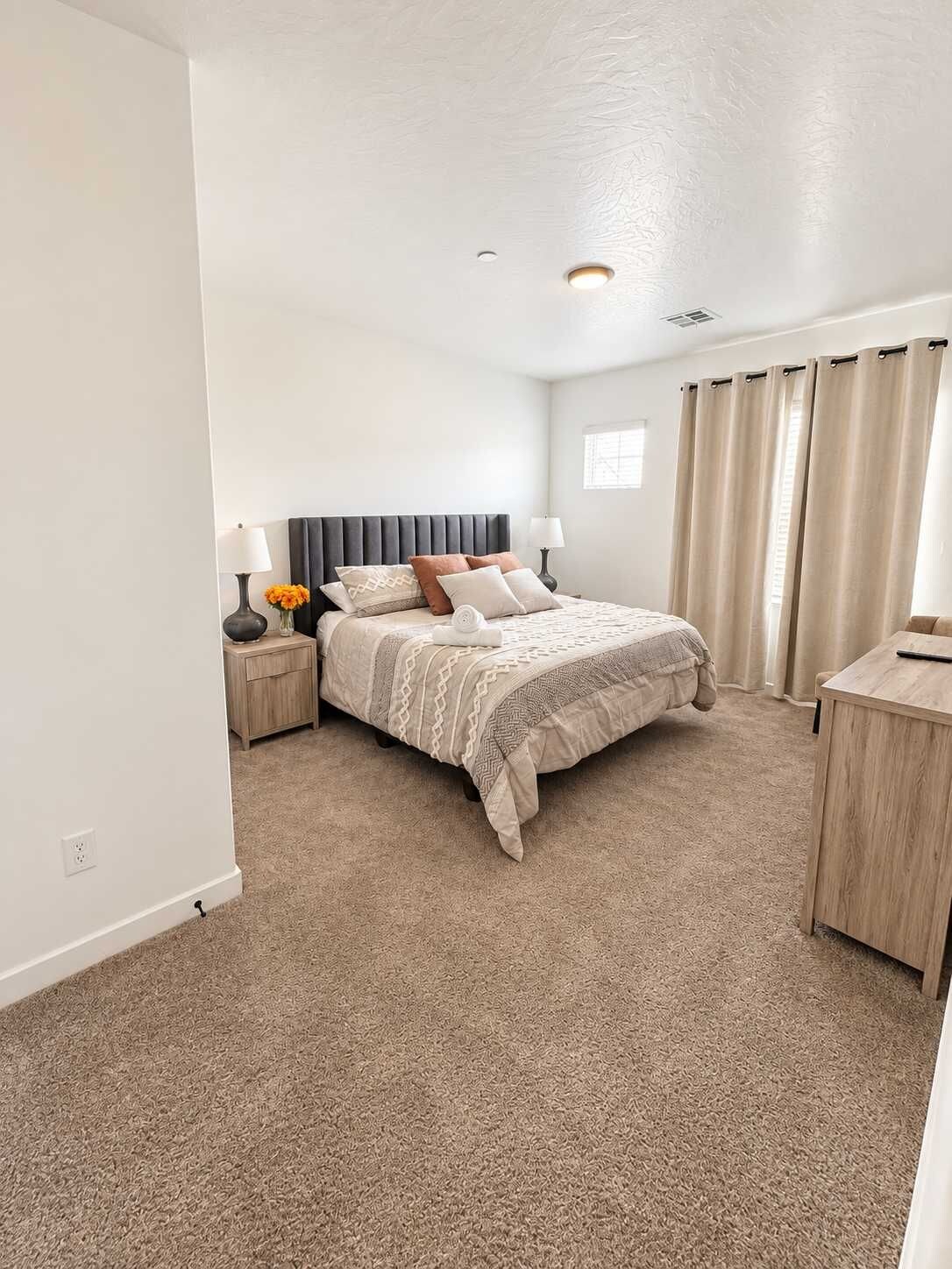 A bedroom with a bed, bedside tables, a desk, and a window with curtains.