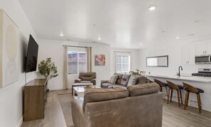 A modern living room with a sofa, coffee table, and TV. There is a kitchen area with a dining table and bar stools. - Long Valley Family Retreat - Sleeps 8 (Washington)