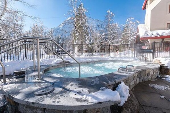 Un bain à remous entouré d’arbres couverts de neige et un bâtiment avec un toit rouge.