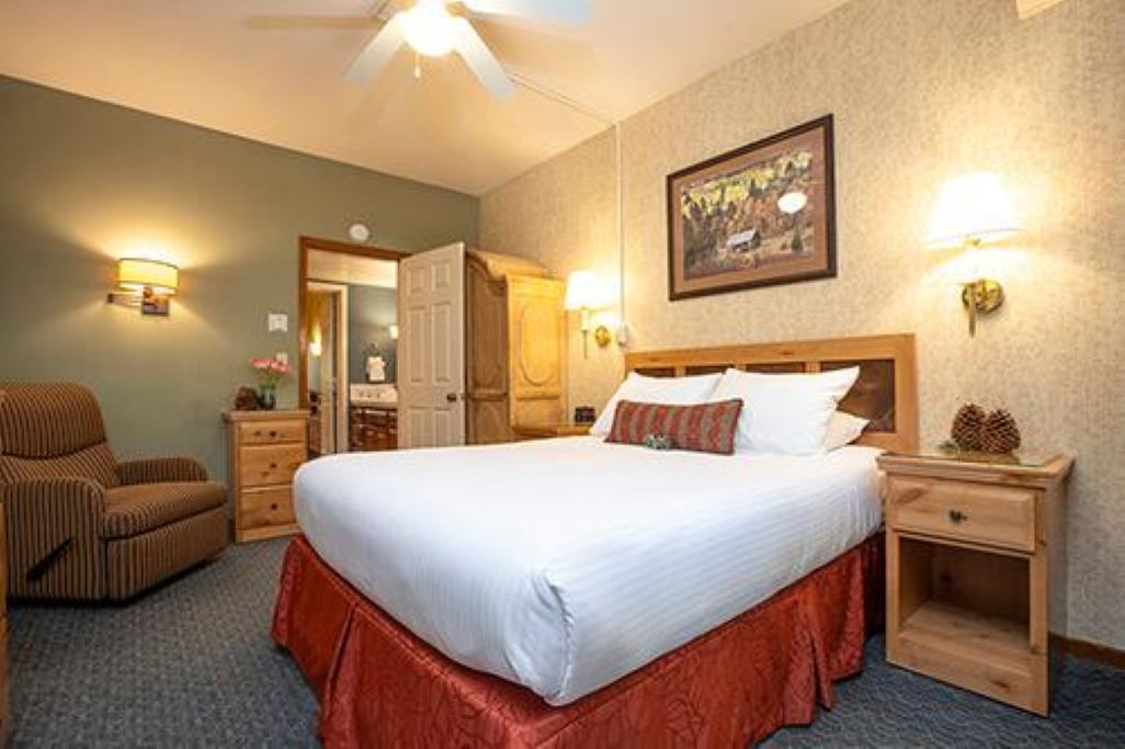 A hotel room with a bed, a chair, a nightstand, and a wall-mounted lamp.