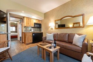 Un salon avec un canapé en cuir marron, une table basse en bois et un coin cuisine doté de meubles en bois et d’un four à micro-ondes.