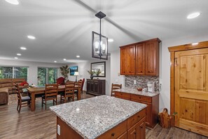 A modern kitchen with granite countertops, wooden cabinets, and a dining area with a red chair. - Cabin Near Brundage | Hot Tub · Outdoor Movies (McCall)