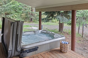 A hot tub on a wooden deck with a covered area, surrounded by trees. - Cabin Near Brundage | Hot Tub · Outdoor Movies (McCall)