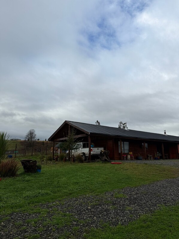 A wooden building with a metal roof, a gravel driveway, and a grassy area with a few plants.