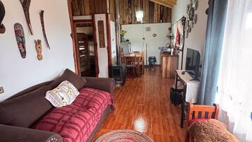 Un salon chaleureux avec un plafond en bois, un canapé, une télévision et un chien.