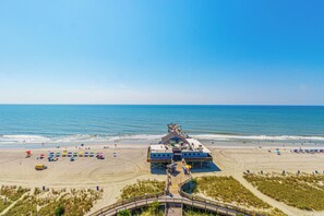 Une jetée au bord de la plage, avec une construction, des parasols de plage et une promenade qui mène à la plage.