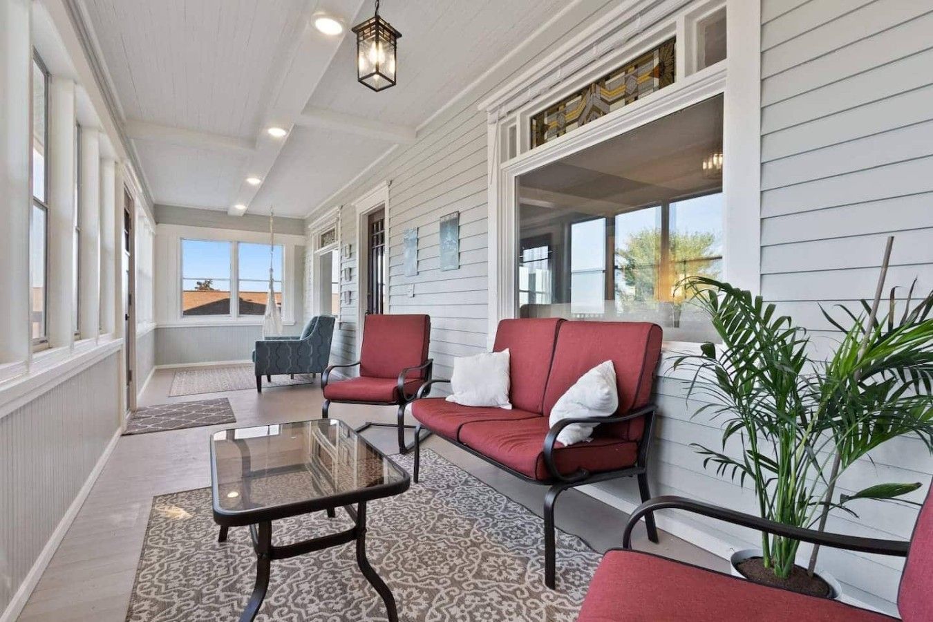 A covered porch with red and grey furniture, a glass table, and a potted plant.