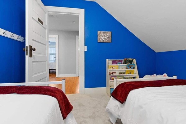 A bedroom with two beds, a bookshelf, and a door leading to another room.