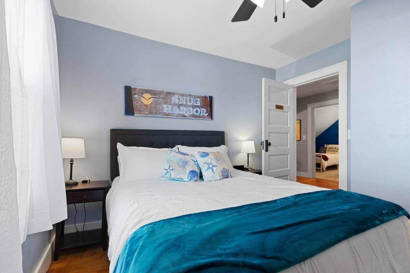 Un dormitorio con cama, dos mesitas de noche, una mesilla, una puerta y un cartel en la pared.