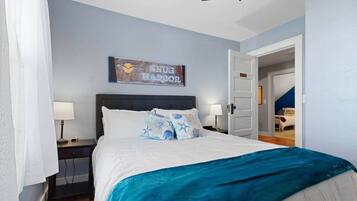 Un dormitorio con cama, dos mesitas de noche, una mesilla, una puerta y un cartel en la pared.