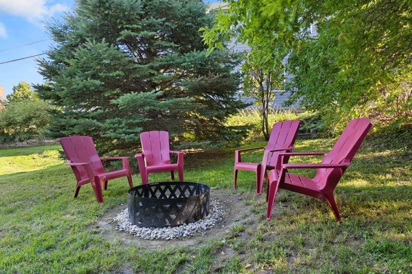 Ein Lagerfeuer mit vier Adirondack-Stühlen, die darum herum in einer grünen Außenanlage angeordnet sind.