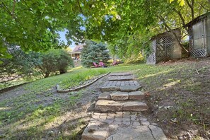 Ein Steinweg führt zu einem Haus mit einem umzäunten Garten und einer überdachten Sitzgelegenheit im Freien.