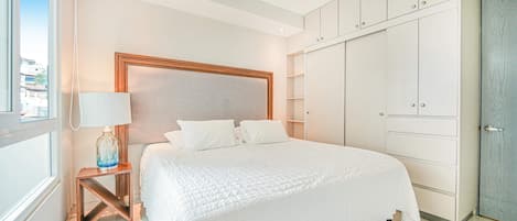 Habitación de hotel con cama, mesita de noche, lámpara, armario y vistas al exterior.