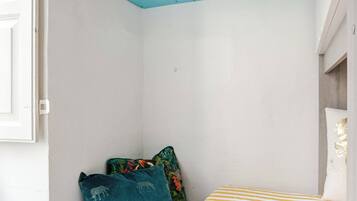 Un dormitorio con una cama, una estantería azul con libros, una ventana y una puerta.