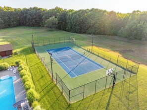 Una pista de tennis envoltada per una tanca, amb una piscina i gandules a prop.