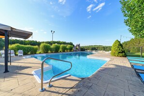 A swimming pool with a metal ladder, surrounded by a paved deck, and a covered seating area.