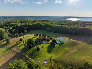 A large property with a tennis court, a swimming pool, and a house surrounded by a forested area.