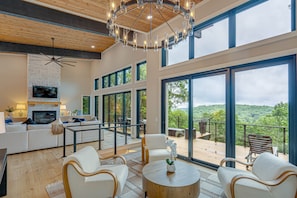 A spacious living area with a fireplace, comfortable seating, and large windows offering a view of the outdoors. - SkySong Cottage | 4BR Mountain View Highlands (Macon County)