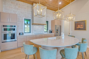 A modern kitchen with a large island, built-in appliances, and a stone accent wall. - SkySong Cottage | 4BR Mountain View Highlands (Macon County)