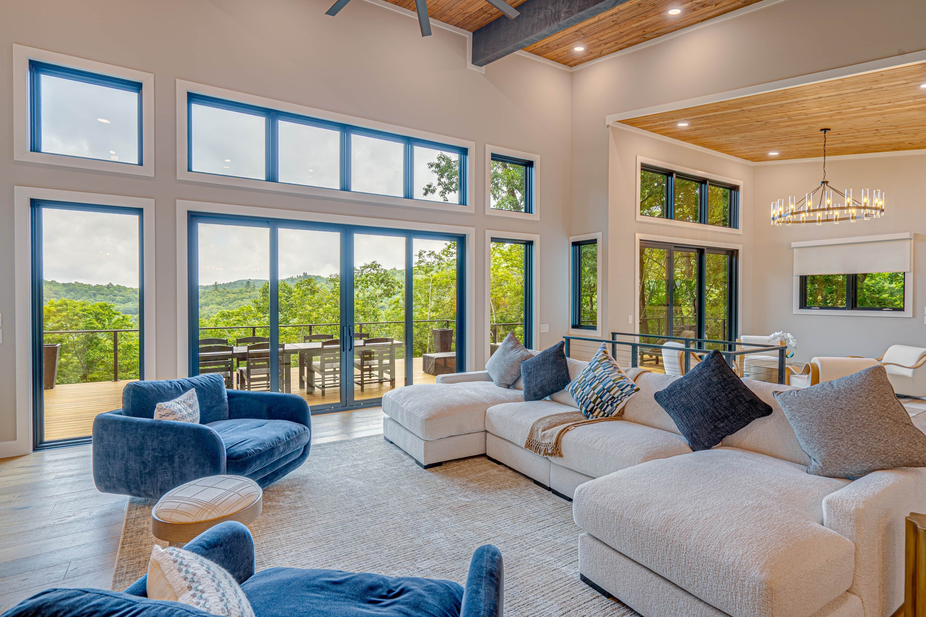 A spacious living area with large windows, a modern chandelier, and a view of the outdoors.