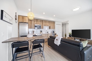 Una cocina moderna con una isla central, sillas negras, un sofá negro y un televisor de pantalla plana.