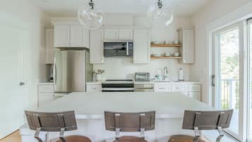 Une cuisine moderne avec des meubles blancs, un îlot central et des luminaires suspendus.