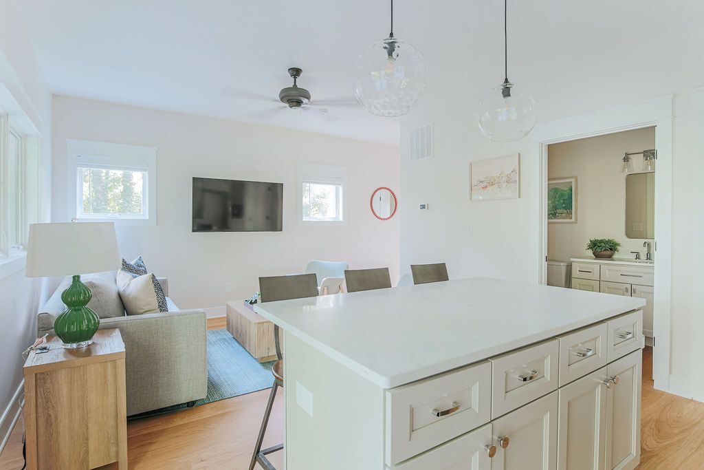 A modern living room with a large white island, a flat-screen TV, and a dining area with chairs.