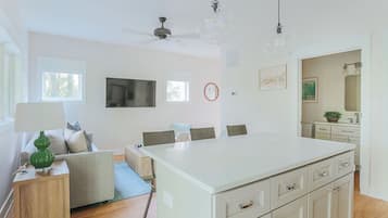 A modern living room with a large white island, a flat-screen TV, and a dining area with chairs.