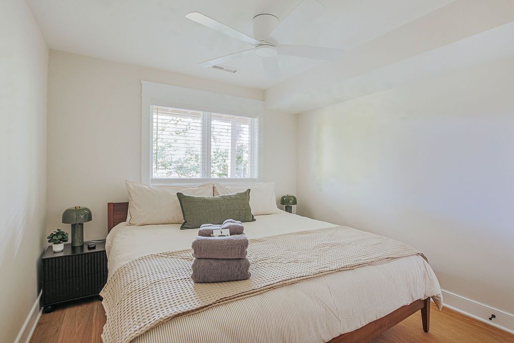 Une chambre à coucher avec un lit, une fenêtre, un ventilateur de plafond et une table de chevet avec une lampe.
