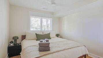 Une chambre à coucher avec un lit, une fenêtre, un ventilateur de plafond et une table de chevet avec une lampe.
