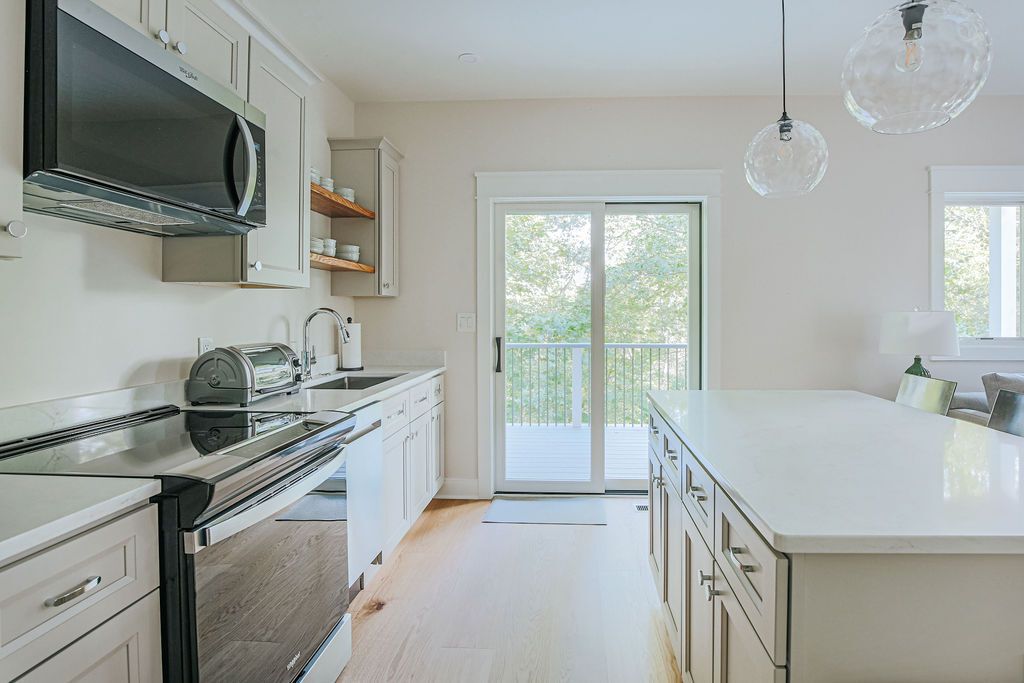 A modern kitchen with a large island, built-in appliances, and a sliding glass door leading to a balcony.