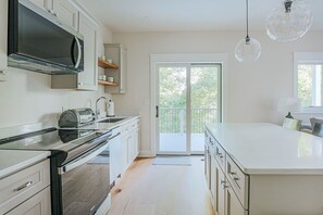 A modern kitchen with a large island, built-in appliances, and a sliding glass door leading to a balcony.