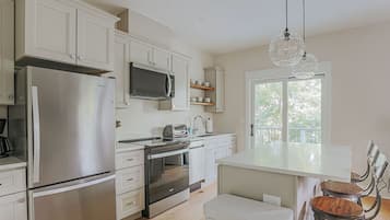 A modern kitchen with stainless steel appliances, white cabinetry, and a large window providing natural light.